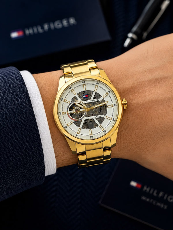 Gold automatic men's watch with 43mm round skeleton dial, stainless steel bracelet, transparent front and back, and self-winding mechanical movement.