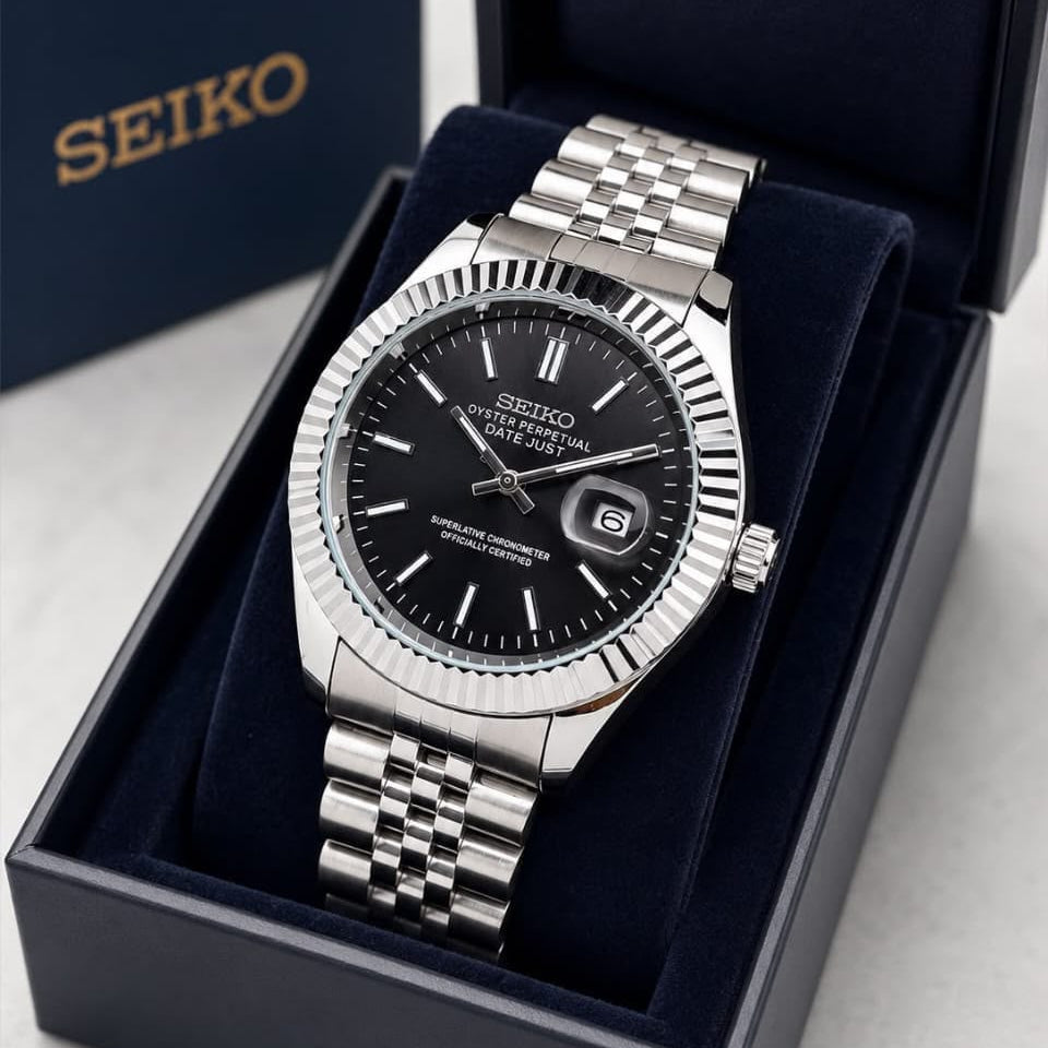 A Seiko stainless steel wristwatch with a black dial and fluted bezel, presented inside an open dark blue Seiko gift box on a light gray surface.