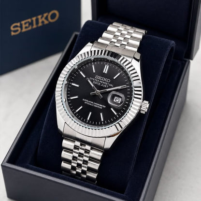 A Seiko stainless steel wristwatch with a black dial and fluted bezel, presented inside an open dark blue Seiko gift box on a light gray surface.