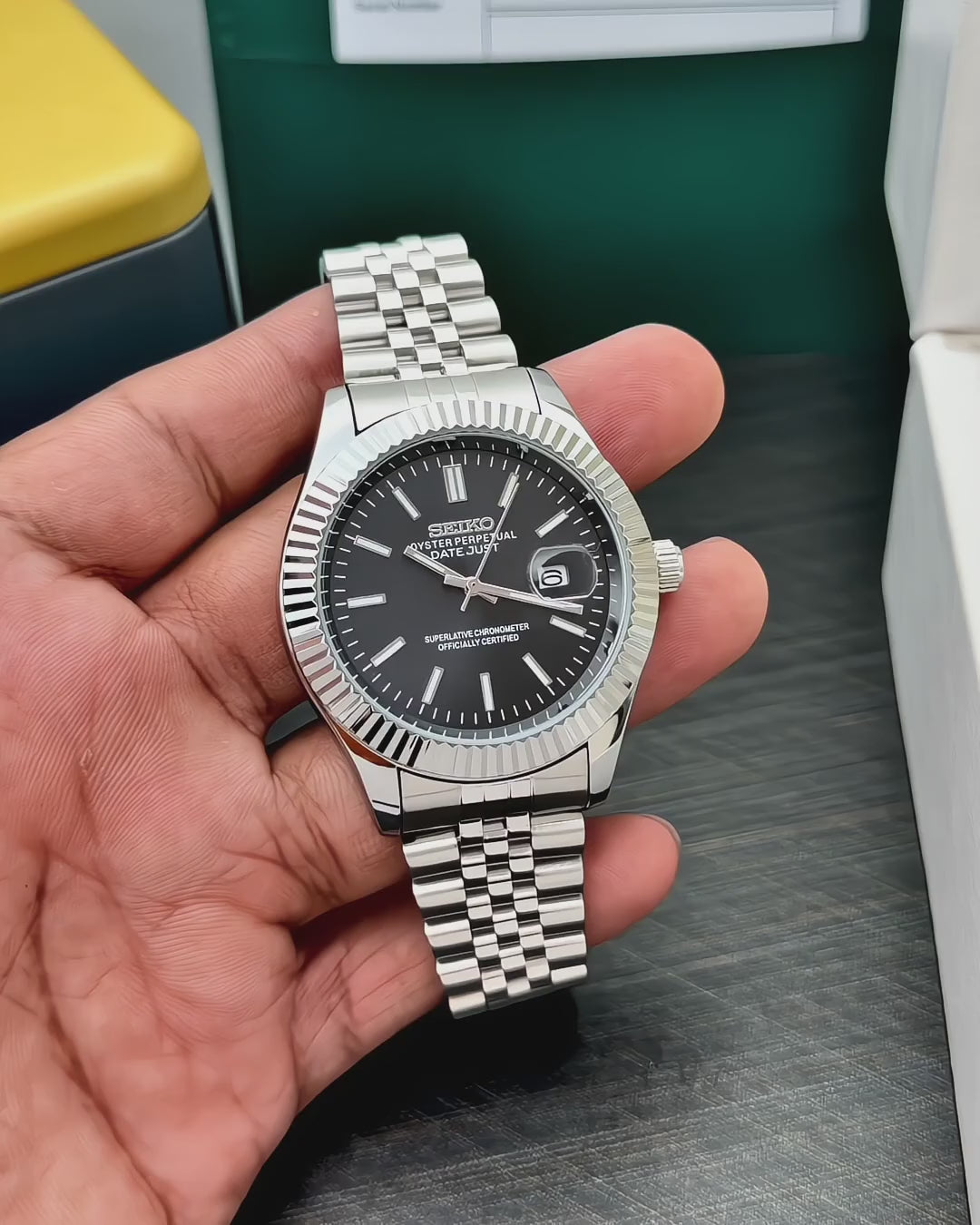 black dial silver stainless steel watch with fluted bezel, magnified date display and multi-link bracelet